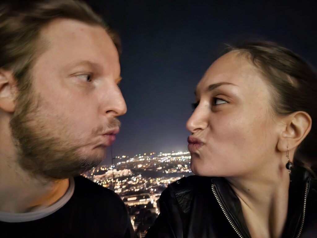 Florian und Eliana einander zugewandt über den Lichtern Athens bei Nacht