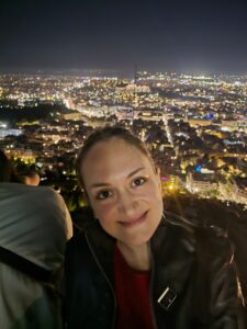 Eliana lächelnd vor dem Lichtermeer Athens